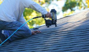 A homeowner measures roof pitch with a level and tape measure inside an attic.