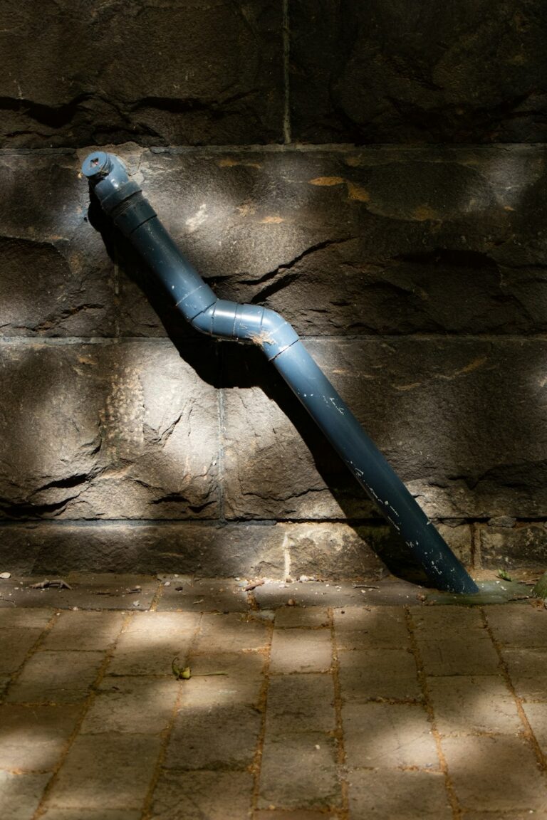 Rainwater flows through a residential gutter and downspout onto a splash block away from the foundation.